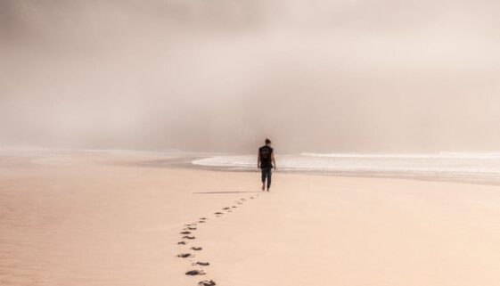 anonymous man walking on sandy seashore in misty weather